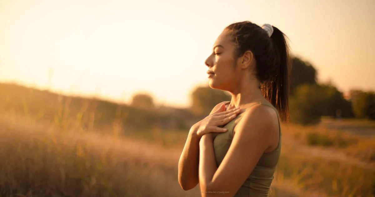 Woman standing on hillside, hands on heart, compassion fatigue recovery through Visionary Somatic Dance, Niio Dance"